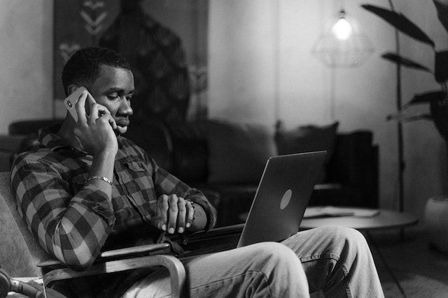 Man wearing flannel on the phone with a laptop.