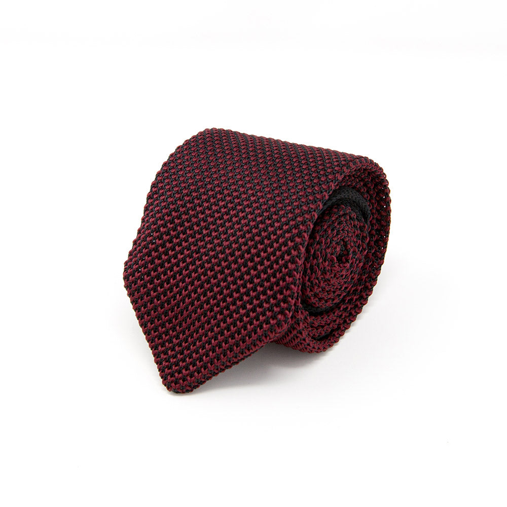 A rolled up burgundy knitted necktie on a white background, demonstrating a casual style with a distinct textured pattern.