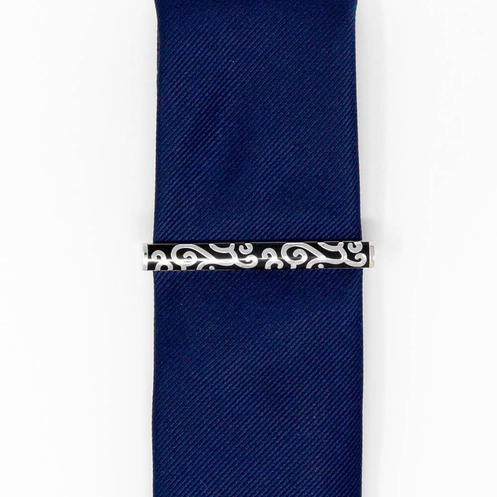 A silver tie clip with a black pattern on a blue navy men's slim tie